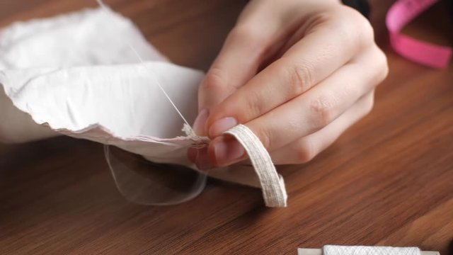 Hands of a young caucasian woman in a sewing thimble from white cotton fabric at night in the house. Making your own reusable protection masks. Close-up view of a woman's hands. Time lapse footage