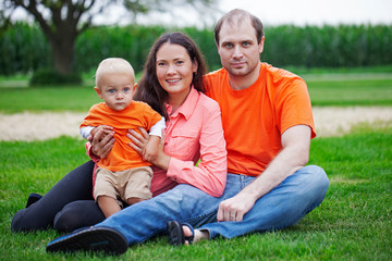 Fototapeta na wymiar Portrait of happy family with little son sitting on grass