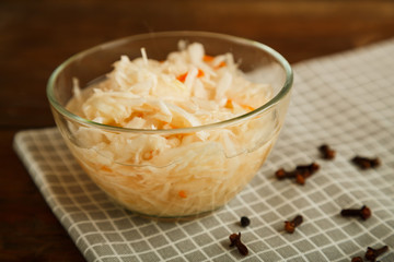 Plate with sauerkraut on a white towel and sprinkled spices on a wooden table.