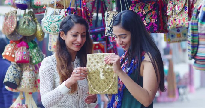 4K Young female friends shopping for handbags in traditional Indian street market. Slow motion.