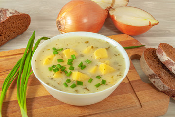 White plate of cheese and potato onion soup surrounded by slices of rye bread, green onions and onions.