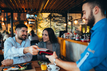 couple in restaurant. man paying contactless with smartphone