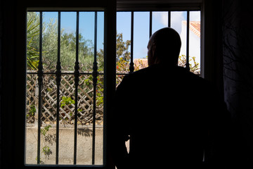 Silhouette of man who is looking through barred window. Restriction due to coronavirus