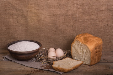 A cut piece of white bread, eggs and flour on a wooden table