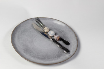 Quail eggs among silver knife and fork on gray plate on white background
