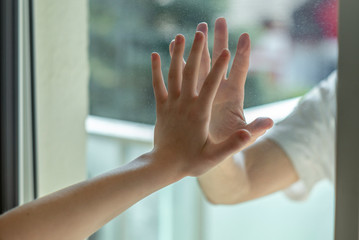 Hands separated by a glass window for social distancing during the corona virus lockdown