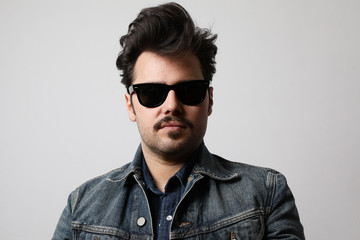 Obraz premium Close-up portrait of serious stylish hipster looks with confident expression, wears sunglasses and denim jacket.