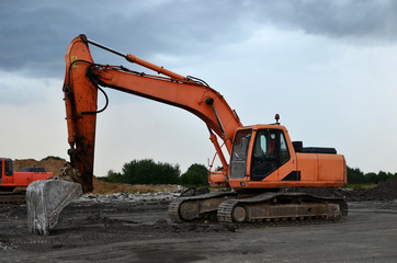 Excavator with a large iron bucket breaks asphalt on a construction site. Demolition work concrete,...