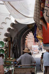 Carrier with Moroccan trolley with straw hat, walking alley with shops on the street, blurred background