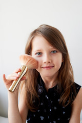 The girl is 6 years old on a light background, powders her cheeks with a brush. Striving for beauty, mother's cosmetics.