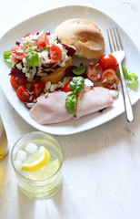 Concetto di cibo. Panino con formaggio, prosciutto, insalata fresca con i pomodori sul piatto bianco. Sfondo bianco. Vista dall'alto.