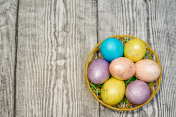 Obraz na płótnie Canvas A basket with many multi colored easter eggs on the wooden background.