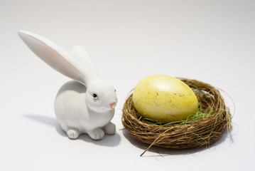 A white bunny rabbit looking at the nest with a yellow easter egg.