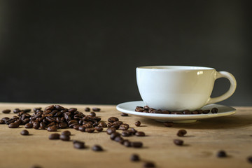 White coffee cup and coffee beans on wooden table with copyspace for text. Selective focus.