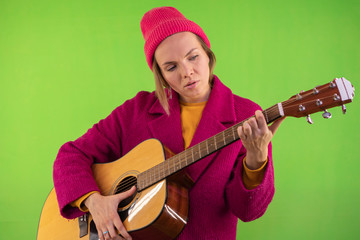 Young and stylish woman with a guitar in a coat and hat on a chromakey background