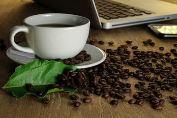 White coffee cup and coffee beans on wooden table with copyspace for text. Selective focus.