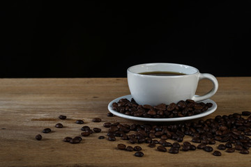 White coffee cup and coffee beans on wooden table with copyspace for text. Selective focus.