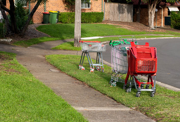 Abandoned shopping trolleys on a green grass near the pathway on a suburb street