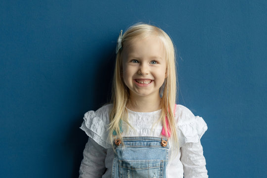 Portrait Of Happy Blonde 4 Years Toddler Girl Indoors Against Blue Wall