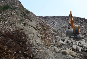 Excavator loads construction waste into reinforced concrete mobile shredder for crushing, recycling of construction mixed waste. Broken concrete recycling at industrial landfill. Screening plant