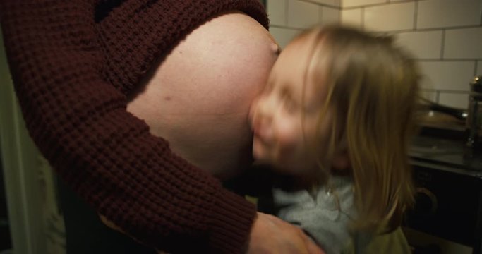 Little boy kissing and rubbing his face against pregnant mother's belly