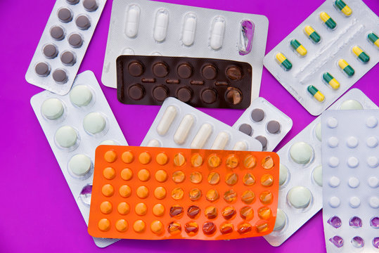 Many colorful tablets and medicines drugs in plastic pharmaceutical packaging on the purple background. Heap of medical pills in package. Concept of healthcare and medicine
