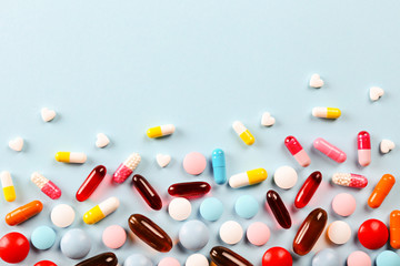 Flat lay composition with bunch of different colorful pills scattered over the table. Pile of opened medication on blue paper textured background. Close up, copy space for text.