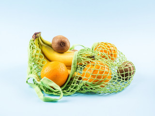Green mesh shopping bag with bananas, kiwi and oranges. Colorful fresh organic fruit. Zero waste concept - plastic free reusable cotton bag