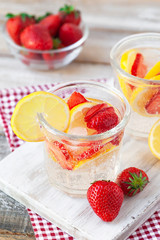Refreshing homemade lemonade with fresh strawberry, lemon and ice. Healthy cold drink, low calories. Tasty cool summer beverage. Wooden white background, two glasses. Macro, close up