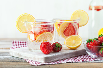 Refreshing homemade lemonade with fresh strawberry, lemon and ice. Healthy cold drink, low calories. Tasty cool summer beverage. Wooden white background, two glasses. Copy space for text