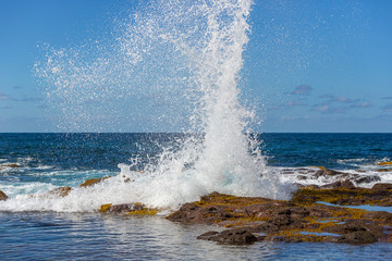A blue wave breaking into the rocks and making a big splash in Tenerife, Canary Islands, Spain