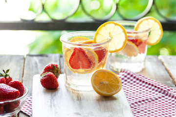 Refreshing homemade lemonade with fresh strawberry, lemon and ice. Healthy cold drink, low calories. Tasty cool summer beverage. Green leaves on background, two glasses. Macro, close up, copy space