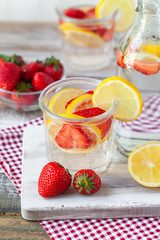 Refreshing homemade lemonade with fresh strawberry, lemon and ice. Healthy cold drink, low calories. Tasty cool summer beverage. Wooden white background, two glasses. Macro, close up