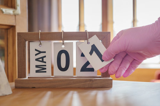 A hand in a latex glove flips the date of May 1 on the folding calendar.