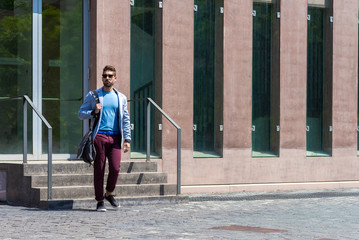 Portrait of a trendy young man walking while holding a shoulder bag