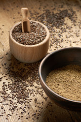Flax seed coarse ground flour in a clay bowl with linseed wooden bowl nearby on rustic wood with grain all around, closeup, copy space, healthy vegan or gluten free food concept
