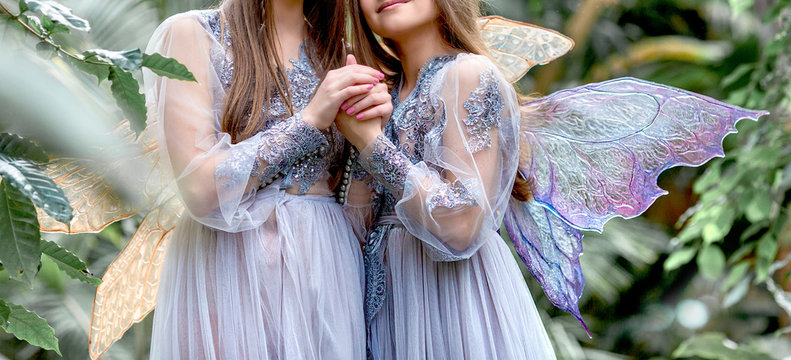 Magical fabulous photo shoot. Two elfs with transparent wings and long blond hair. Beautiful young girls in a silver-purple dress enjoys nature in a botanical garden. Magic and magic. Special effects