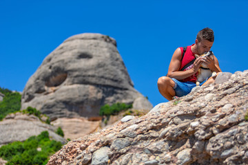 A squatting young man and his dog at the top of Montserrat mountain, Barcelona