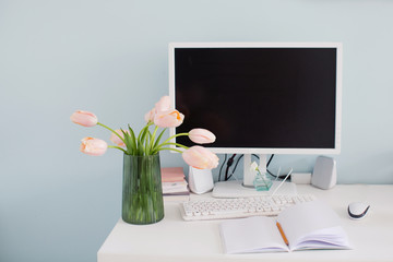 Modern workplace in light room with blue walls. Bouquet of pink tulips on the table