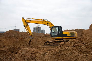 Excavator during earthworks at construction site. Backhoe digging the ground for the foundation and for laying sewer pipes district heating. Earth-moving heavy equipment