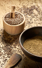 Flax seed coarse ground flour in a clay bowl with linseed wooden bowl nearby on rustic wood with grain all around, closeup, copy space, healthy vegan or gluten free food concept