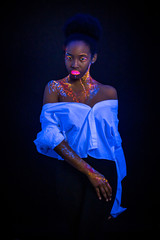 african woman with body art glowing in ultraviolet light. Portrait of beautiful woman painted in fluorescent powder. isolated dark space