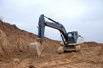Excavator during earthworks at construction site. Backhoe digging the ground for the foundation and for laying sewer pipes district heating. Earth-moving heavy equipment