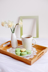 Wooden breakfast tray with a bouquet of spring flowers in bed .a Cup of morning tea with macaroons and a flower