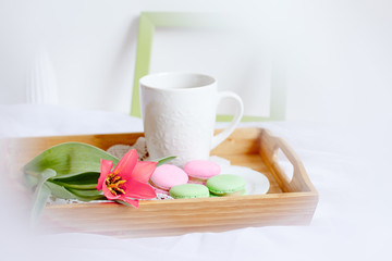 Wooden breakfast tray with a bouquet of spring flowers in bed .a Cup of morning tea with macaroons and a flower