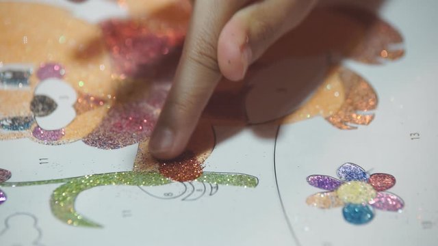 The child paints the paper drawings with shiny powder, rubbing small glitters on the basis of glue. Develops children's creativity