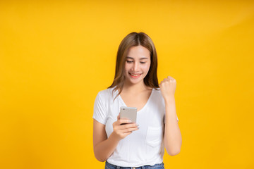 Portrait happy young asian woman glad lucky and successful with holding smartphone mobile positive emotion in white t-shirt, Yellow background isolated studio shot and copy space.