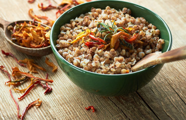 Buckwheat porridge cooked and garnished with vegetables and herbs: sweet red pepper, dill and rosemary on wood, closeup, copy space, healthy vegetarian protein food concept