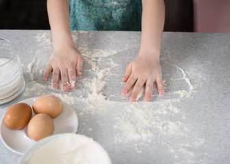 Funny cute little girl preparing dough in the kitchen. Child bakes cookies in the kitchen at home.