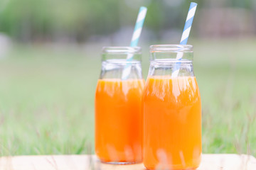 Closeup glass bottle of orange juice fruit on green grass nature background, food healthy concept